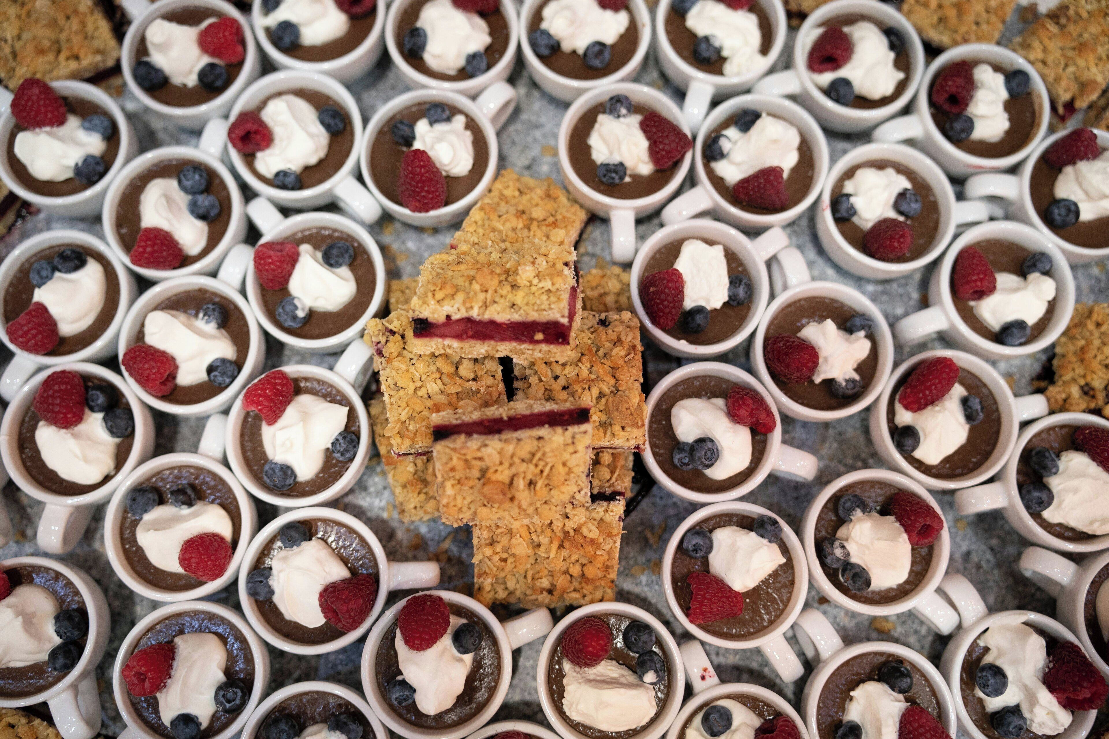A dessert arrangement with multiple cups of chocolate mousse topped with whipped cream and berries, surrounded by a large square of granola.