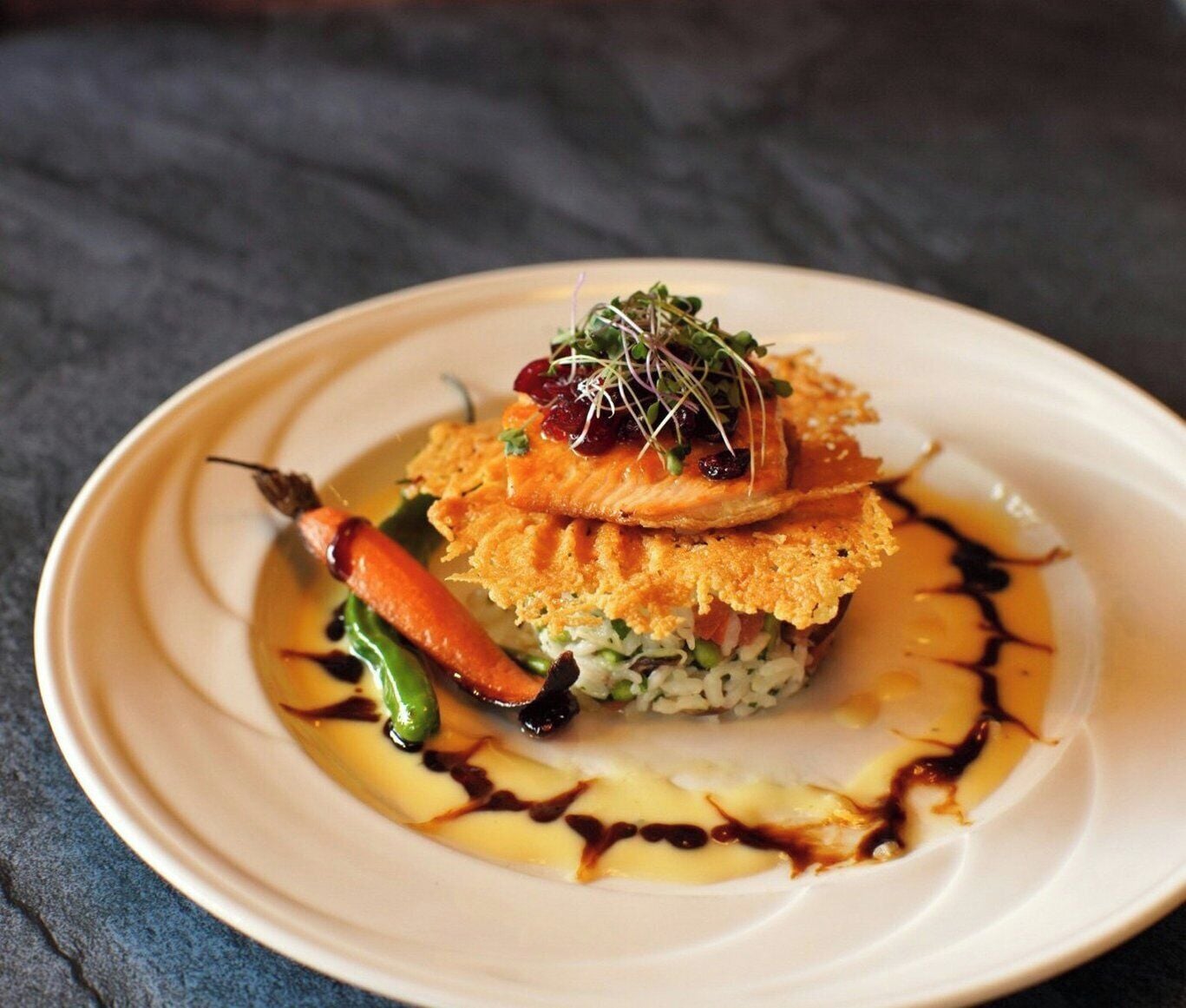 A plate with a layered dish, possibly salmon, garnished with microgreens and a cherry.