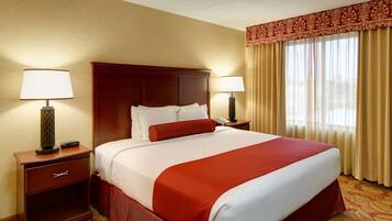 A hotel room with a large bed, two bedside tables with lamps, a wooden headboard, and a window with curtains.