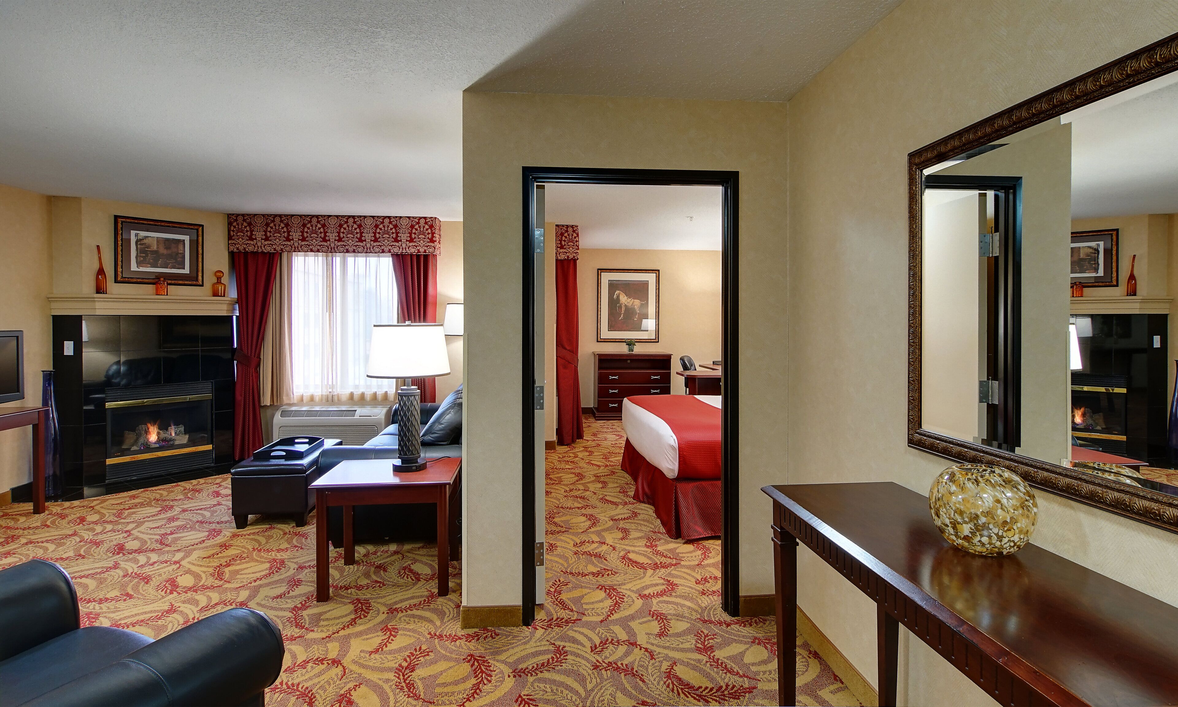 Een hotelkamer met een open haard, een bed, een bureau en een grote spiegel.
