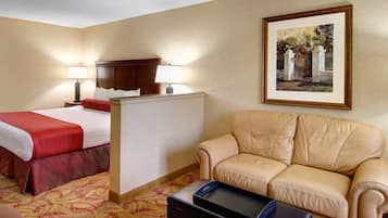 A hotel room with a bed, a sofa, a desk with a lamp, and a framed picture on the wall.