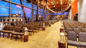 A spacious hall with rows of chairs and tables, large windows, and a wooden ceiling.