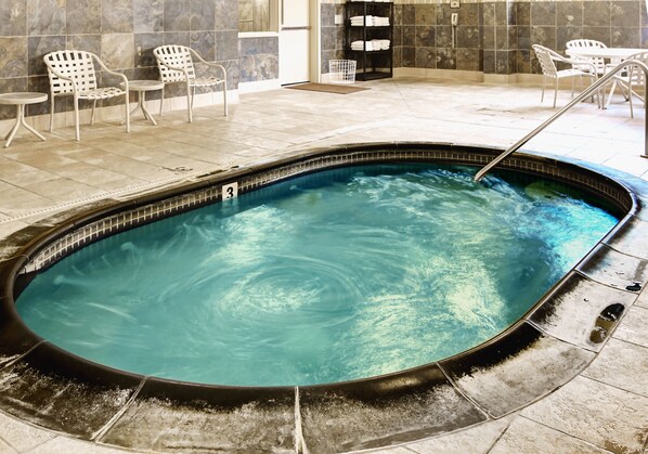 A hot tub with a tiled floor and a metal railing. There are white chairs and a small table in the background.