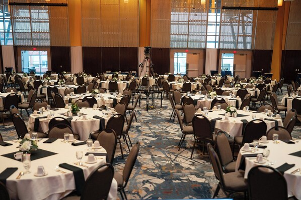 A large banquet hall with multiple round tables set for dining, arranged in rows.