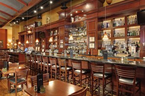 A bar area with wooden chairs and tables, a bar counter, and shelves stocked with bottles and glasses.