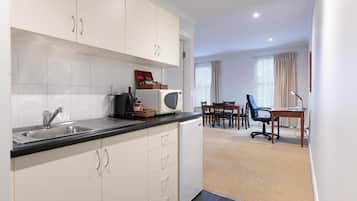 A modern kitchen with white cabinets, a black countertop, and a microwave. There is a dining area with a table and chairs, and a carpeted floor.