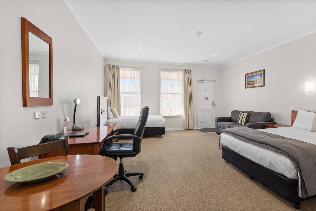 A hotel room with a bed, a desk with a chair, a sofa, and a dining table.