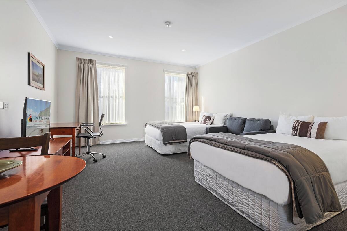 A hotel room with two beds, a desk, a chair, and a refrigerator.