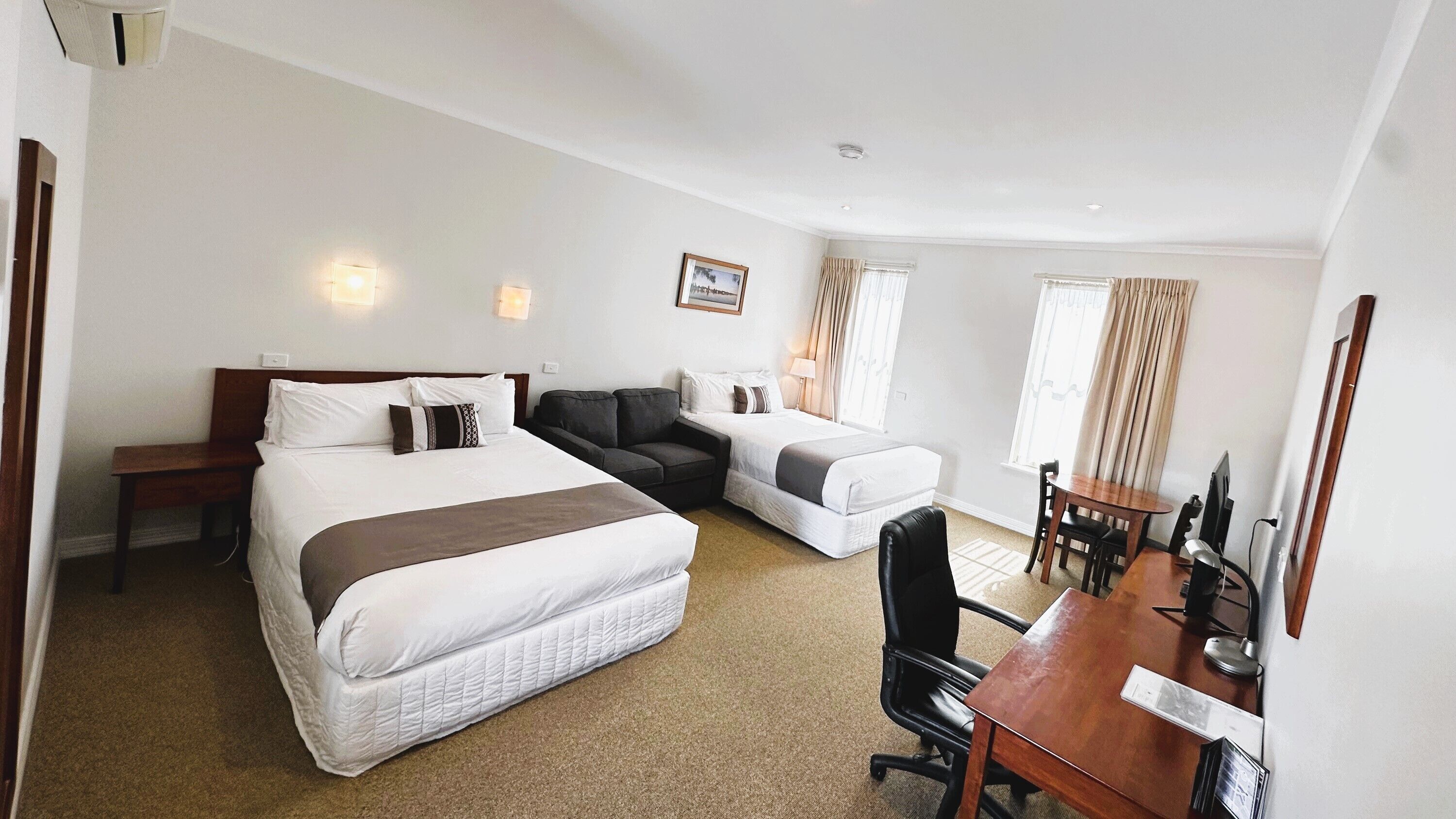 A hotel room with a large bed, a sofa, a desk with a chair, and a dining table.