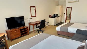 A hotel room with a TV, desk, chair, kitchenette, and two beds.