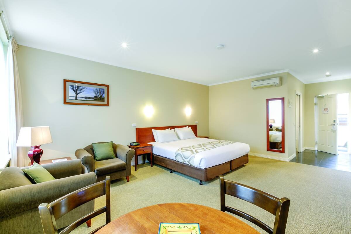A hotel room with a bed, two armchairs, a table, a lamp, and a picture on the wall.