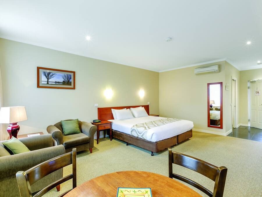 A hotel room with a bed, two armchairs, a table, a lamp, and a picture on the wall.