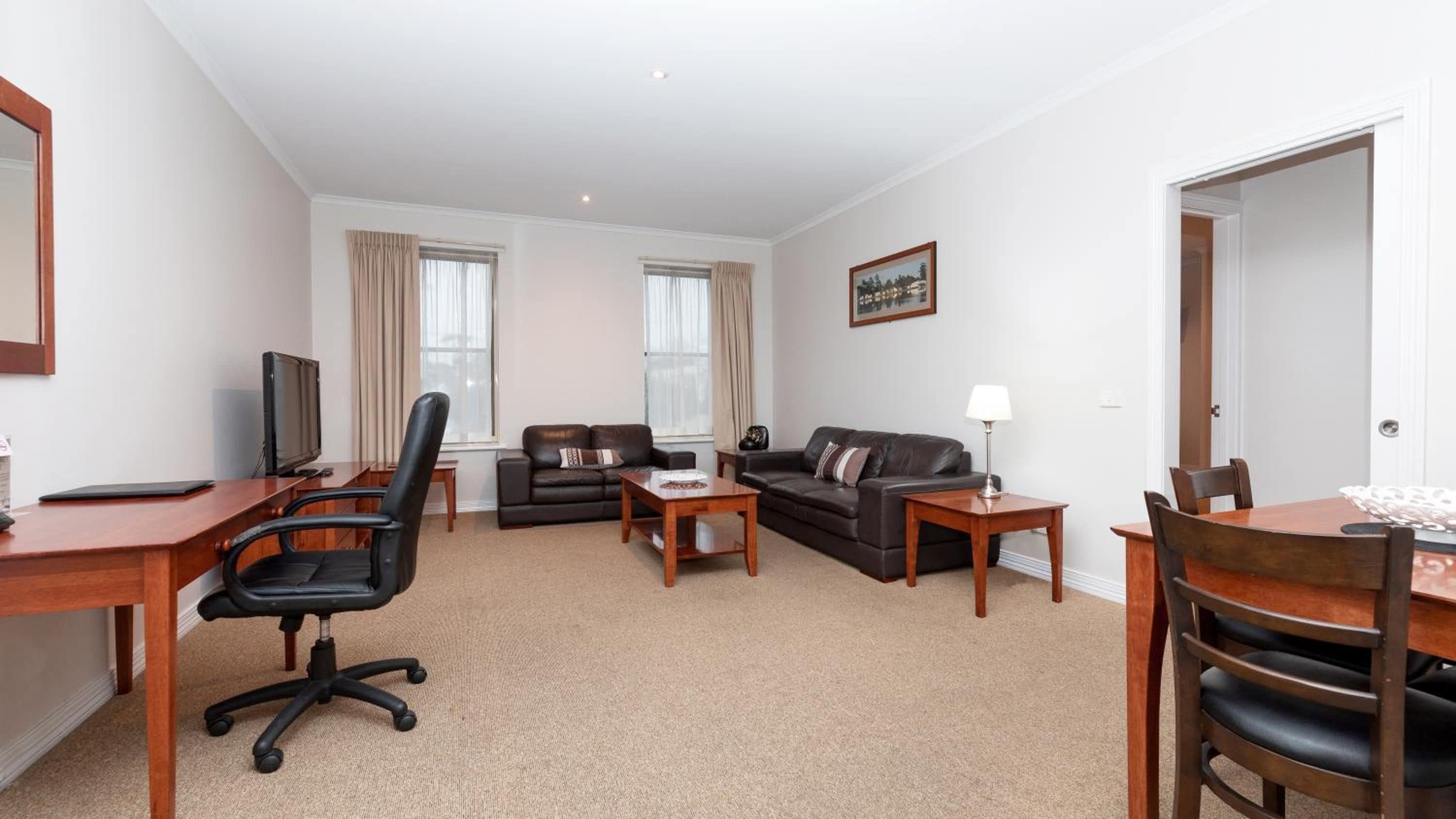 A furnished living room with a desk, office chair, two sofas, a coffee table, and a dining table with chairs.