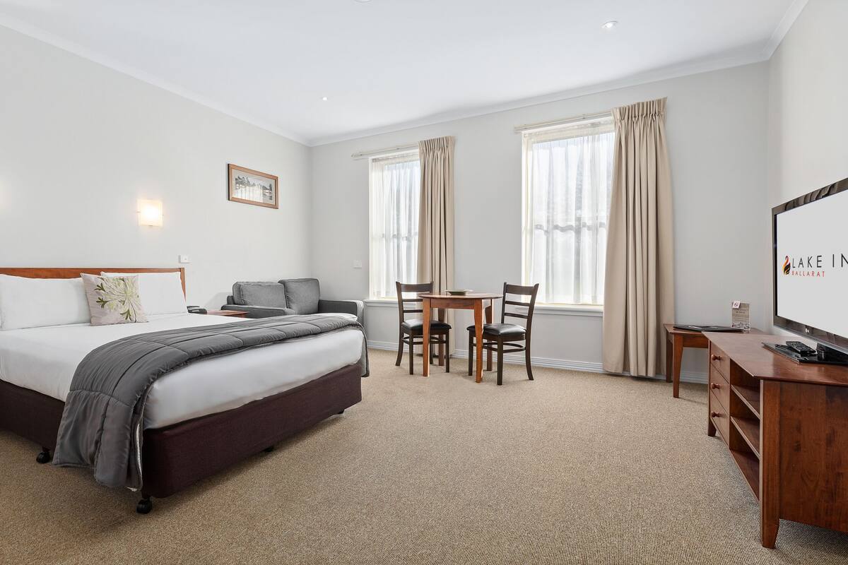 A hotel room with a bed, bedside table, desk, chair, and a TV.