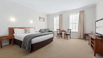 A hotel room with a bed, bedside table, desk, chair, and a TV.