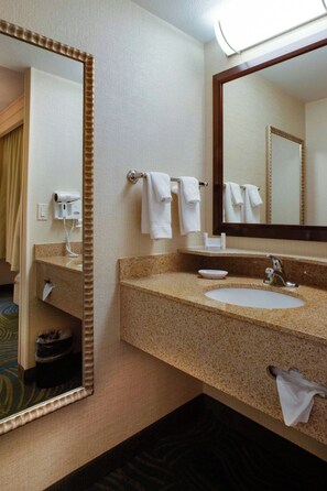 A hotel bathroom with a granite countertop sink, a large mirror, and a hairdryer on the wall.