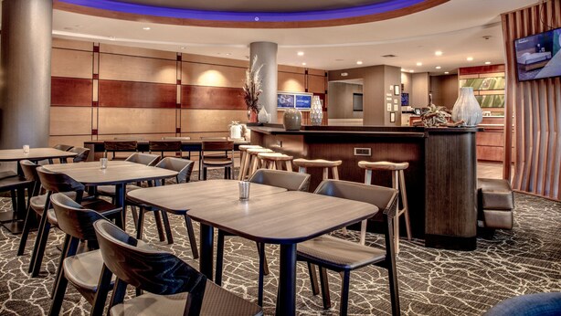 A hotel lobby with multiple tables and chairs, a reception desk, and a television screen. - SpringHill Suites by Marriott Savannah Airport (Savannah)