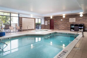 A swimming pool with a hot tub, lounge chairs, and a brick wall.