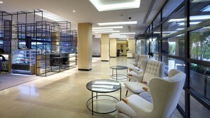 Un hall d’hôtel moderne, doté d’espaces détente, d’un comptoir d’accueil et d’une cuisine visible à travers une paroi en verre.