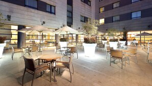 An outdoor patio area with tables and chairs, umbrellas, and potted plants. - Exe Madrid Norte (Madrid)