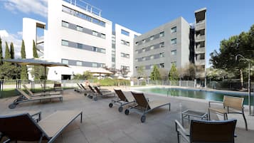 Un hotel moderno con piscina en la azotea, tumbonas y una vista despejada a la piscina.