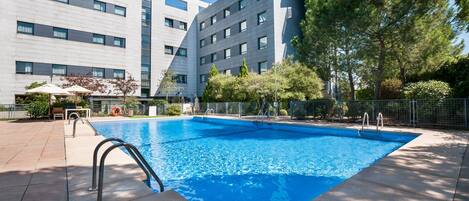 A modern hotel with a swimming pool, outdoor seating, and a clear blue sky.