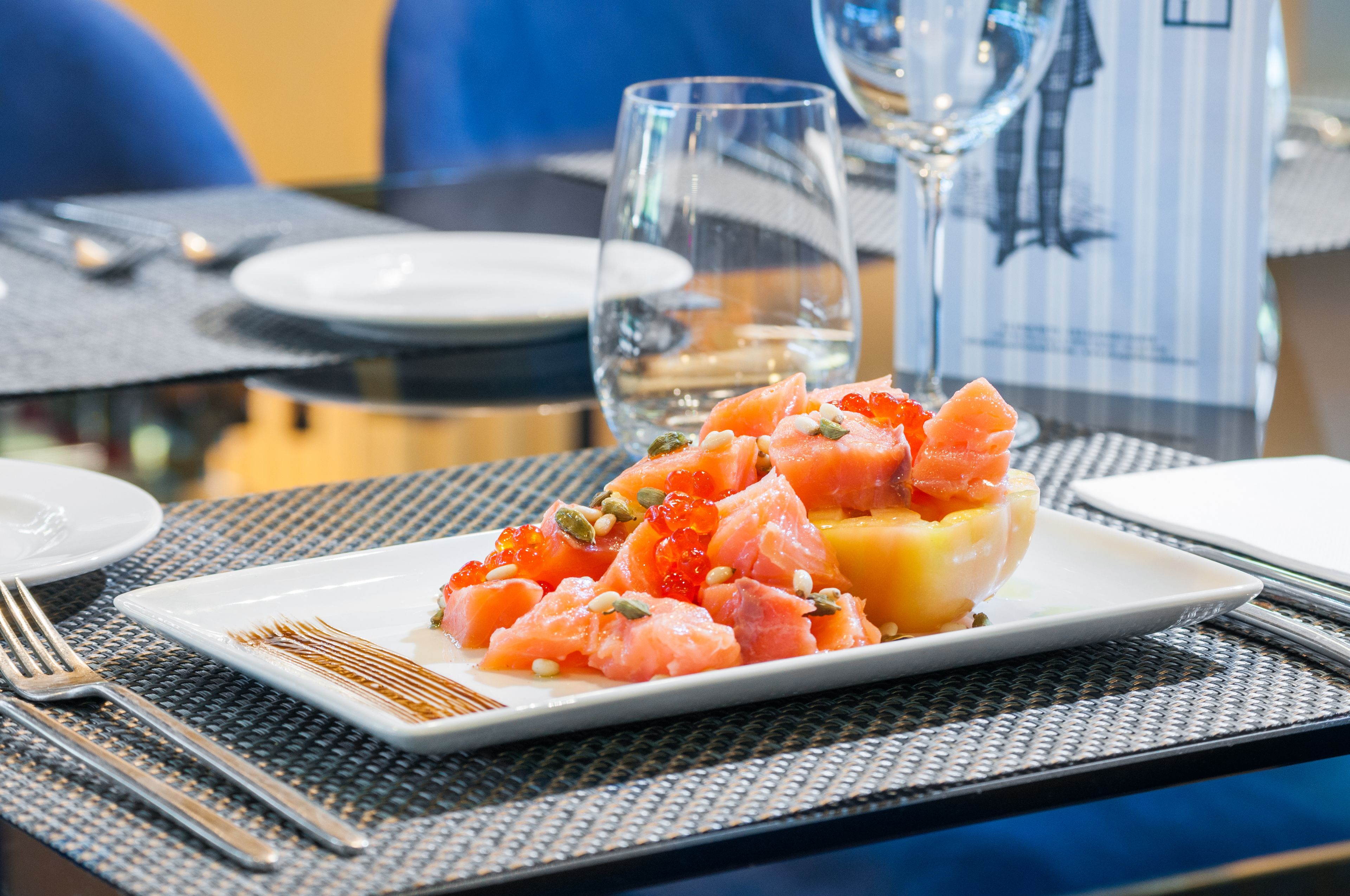Una mesa de comedor con una porción de tártaro de salmón en un plato blanco, un vaso de agua y una copa de vino.