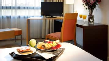 Habitación de hotel con una mesa de comedor dispuesta para el desayuno, una televisión y un jarrón con flores.