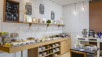 A modern kitchen with a buffet setup, including a chalkboard menu, shelves with kitchenware, and a dining area with a table set for two.