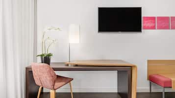 Una camera d'albergo moderna con una scrivania in legno, una sedia rossa, una TV e una pianta in vaso.