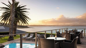 A poolside area with wicker furniture and a view of the ocean at sunset. - Protea Hotel by Marriott Mossel Bay (Mossel Bay)