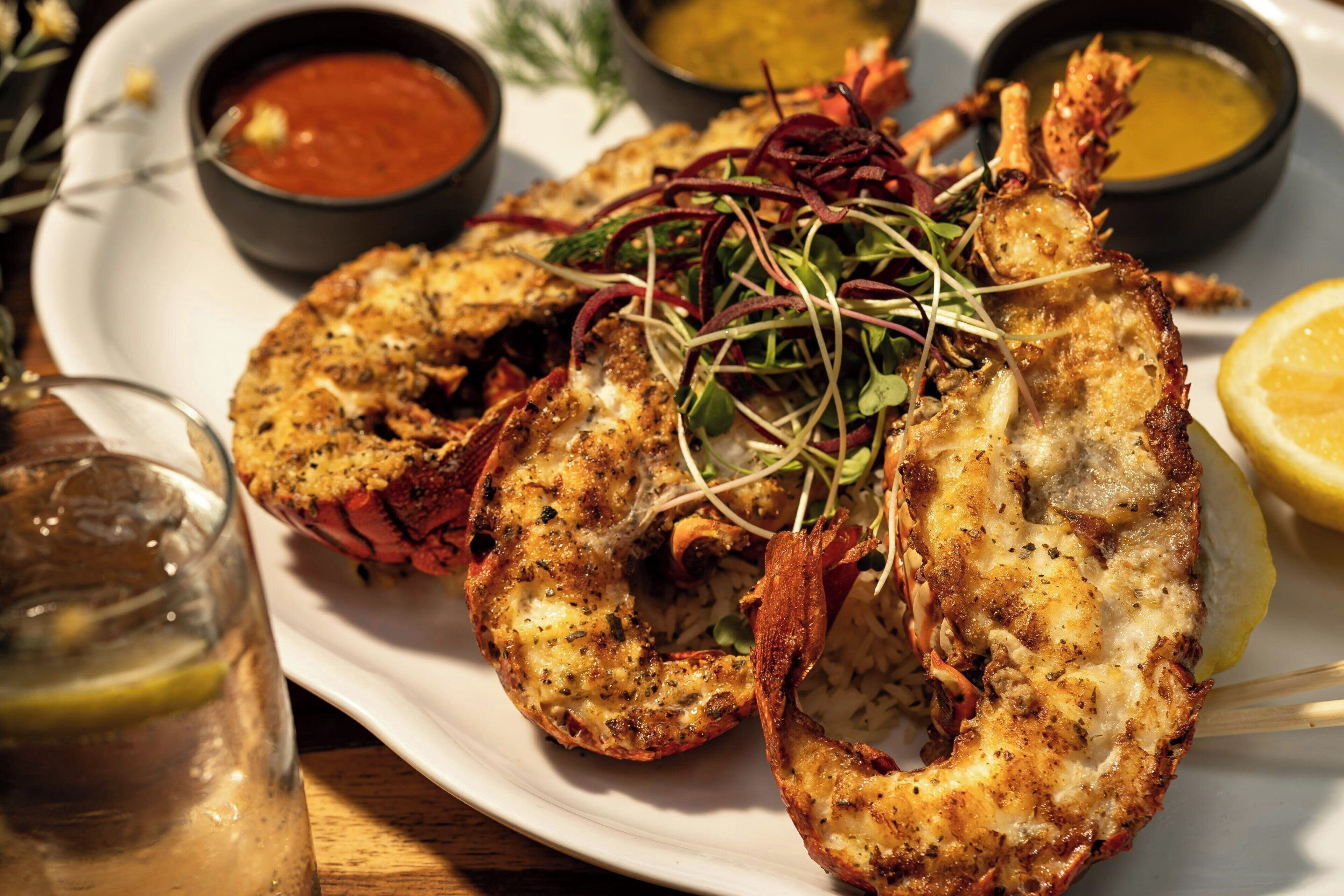 A plate of grilled lobster with a lemon wedge and two dipping sauces.