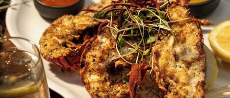 A plate of grilled lobster with a lemon wedge and two dipping sauces.