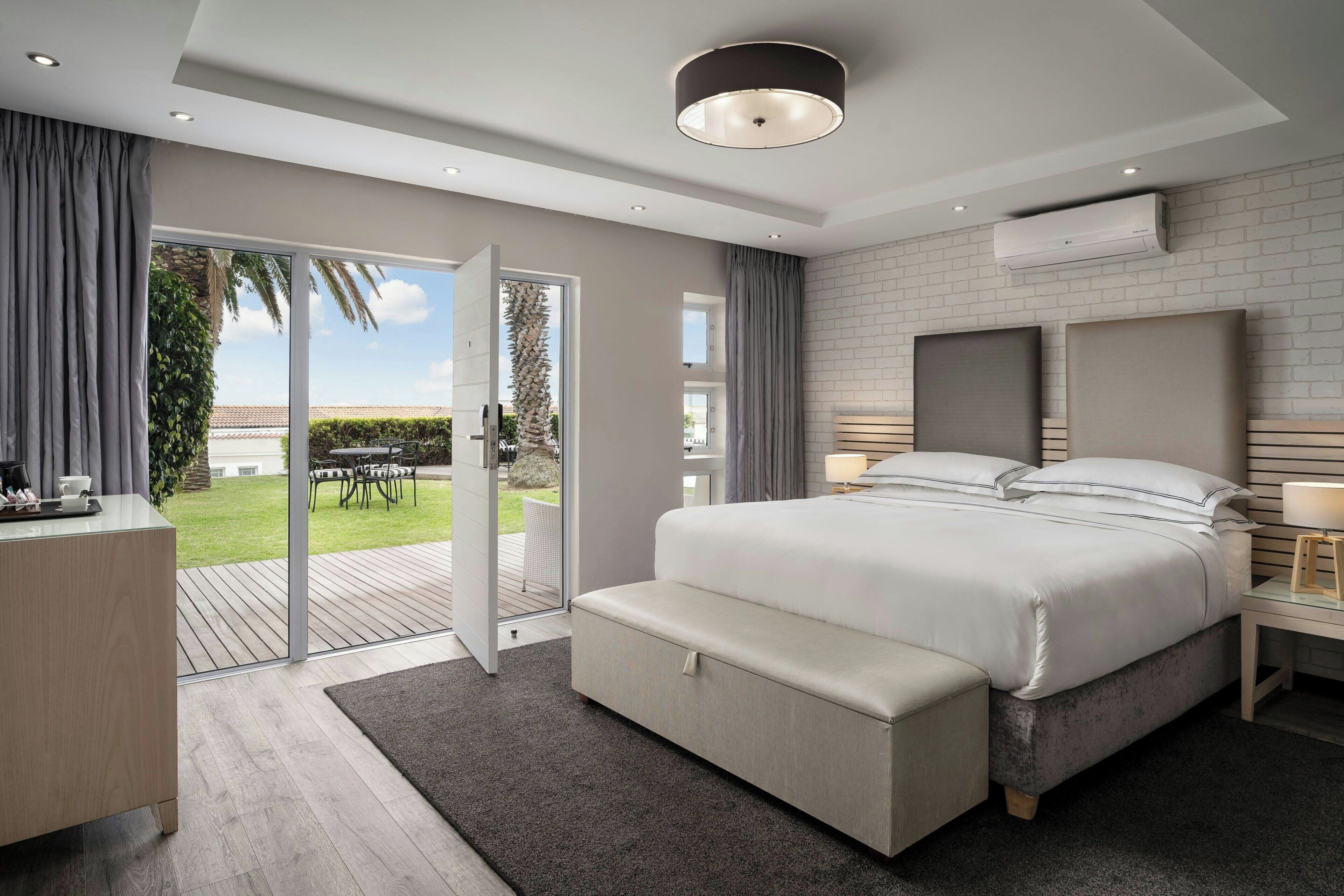 A modern bedroom with a large bed, bedside tables, a desk, and a sliding glass door leading to a patio.
