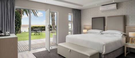 A modern bedroom with a large bed, bedside tables, a desk, and a sliding glass door leading to a patio.
