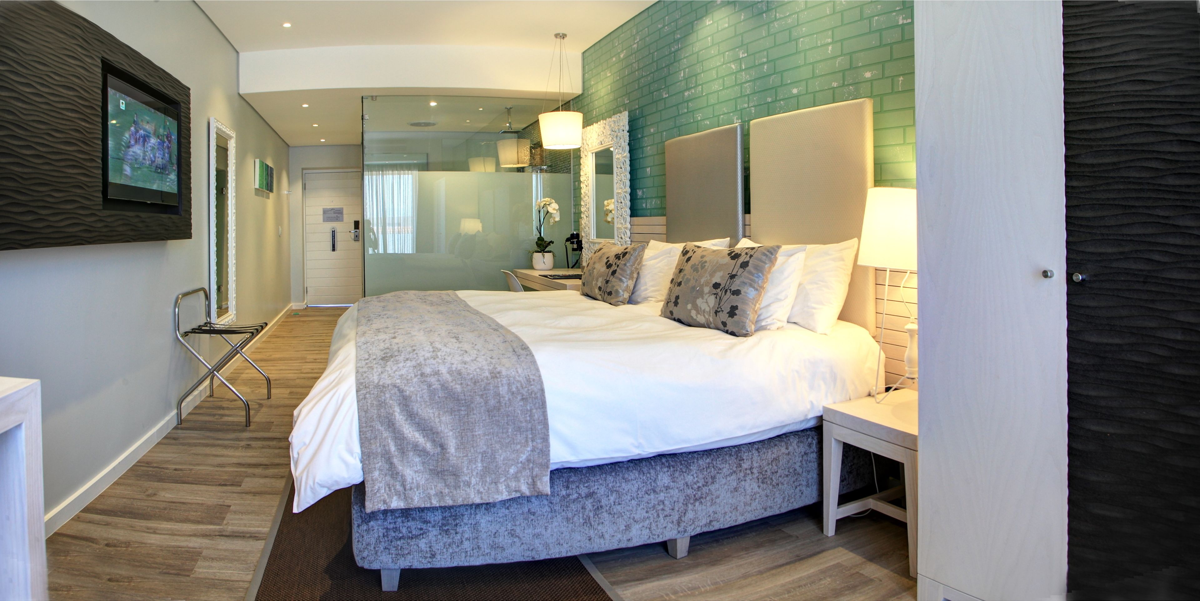 A modern hotel room with a large bed, a bedside table, a mirror, and a TV mounted on the wall.