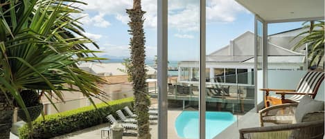 A modern outdoor pool area with lounge chairs, a glass-enclosed patio, and a view of the ocean.