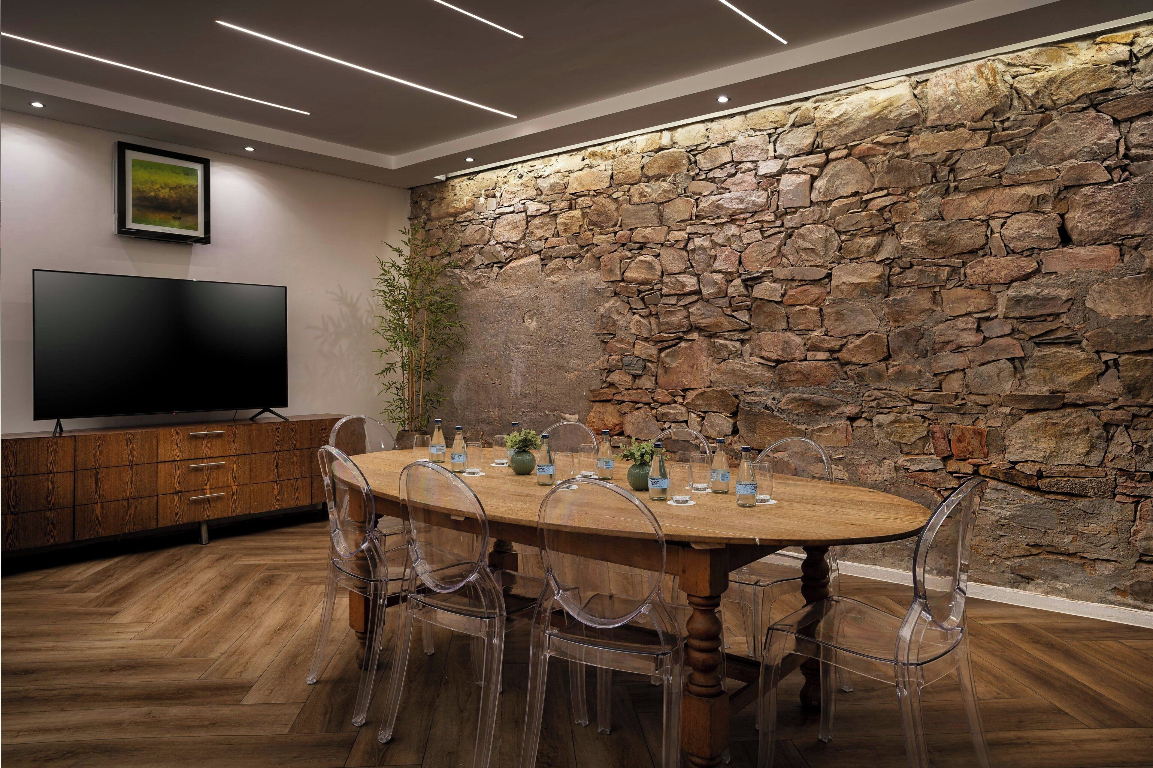A dining area with a stone wall, wooden table, clear chairs, and a flat-screen TV.