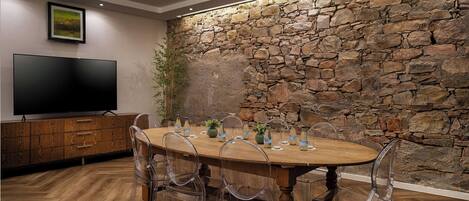 A dining area with a stone wall, wooden table, clear chairs, and a flat-screen TV.