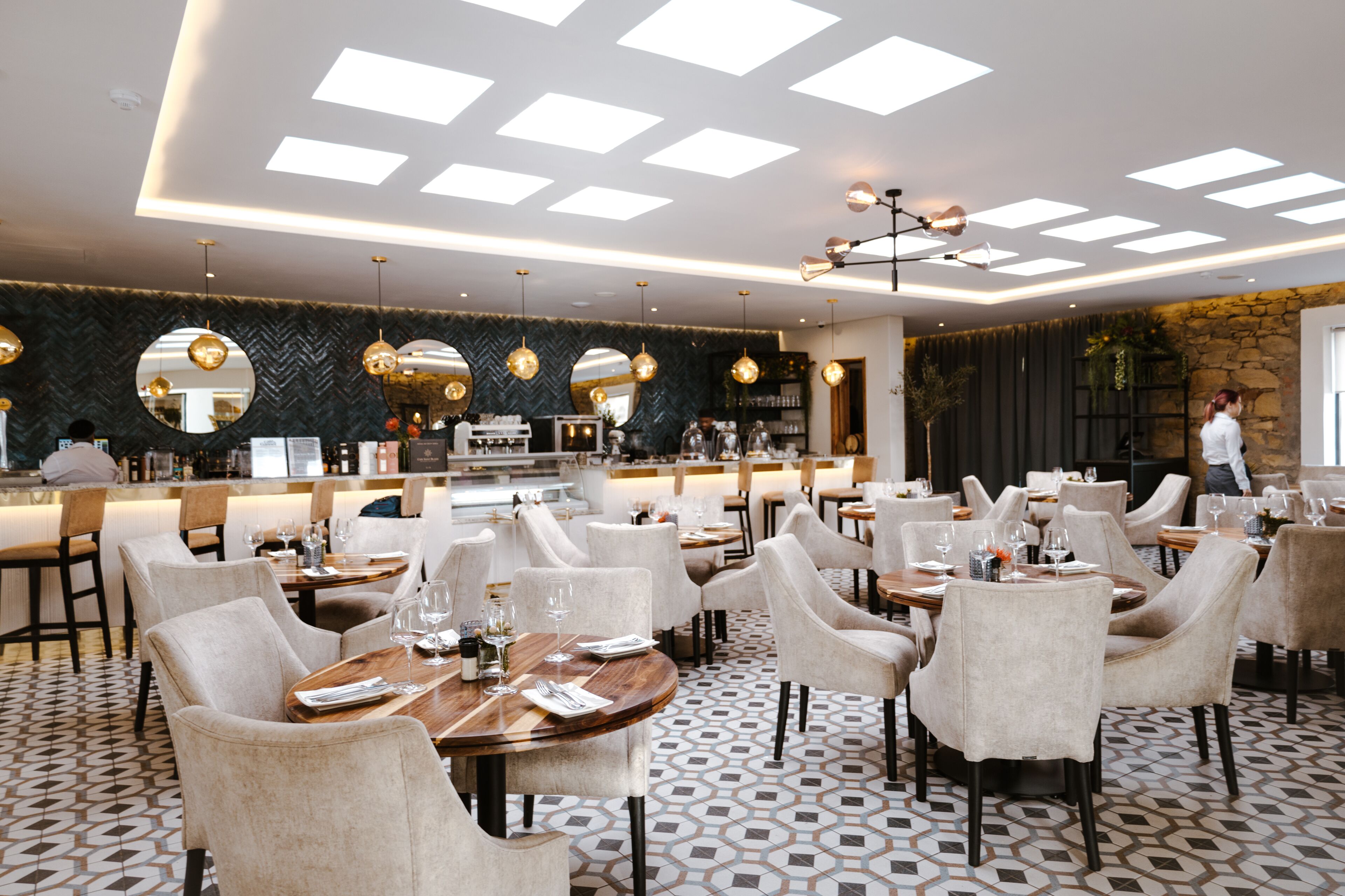 Ein modernes Restaurant mit hoher Decke, einem geometrisch gemusterten Boden und runden Tischen mit Stühlen.