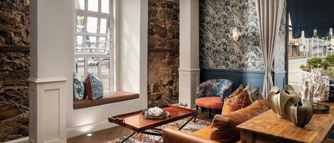 A cozy living room with a stone wall, a bench with cushions, a patterned rug, and a wooden table with decorative items.