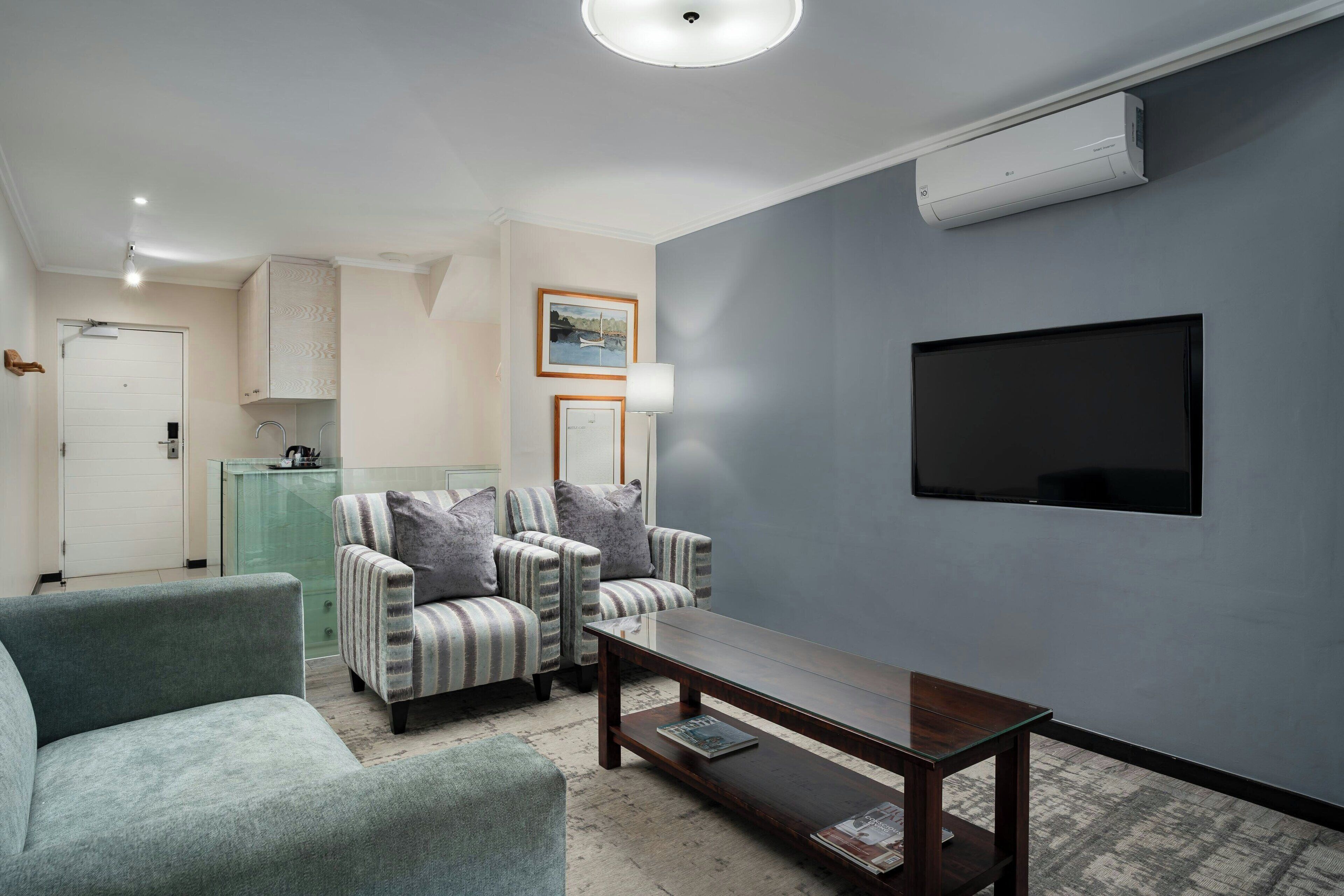 Una sala de estar con una pared gris, un televisor de pantalla plana, dos sillones a rayas, un sofá verde y una mesa de centro de madera.