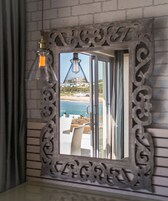 Un espejo con un marco decorativo que refleja una vista de la playa, una lámpara colgante y una puerta que da a un espacio exterior.
