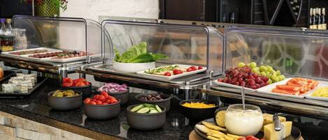 Un buffet proposant une variété de plats, notamment des salades, des fruits, des fromages et des sauces.