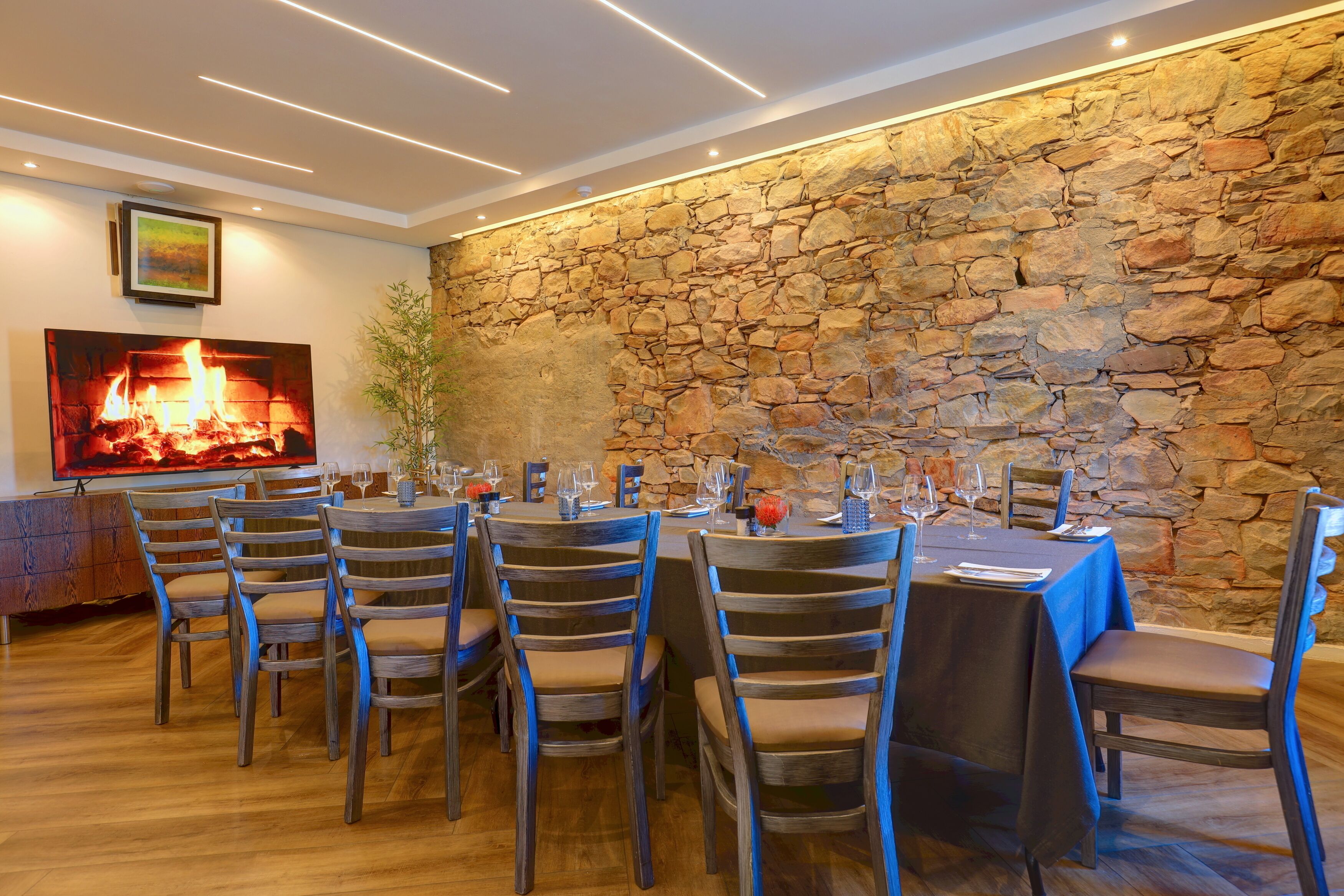 Un comedor con pared de piedra, sillas de madera y una mesa dispuesta para seis personas.