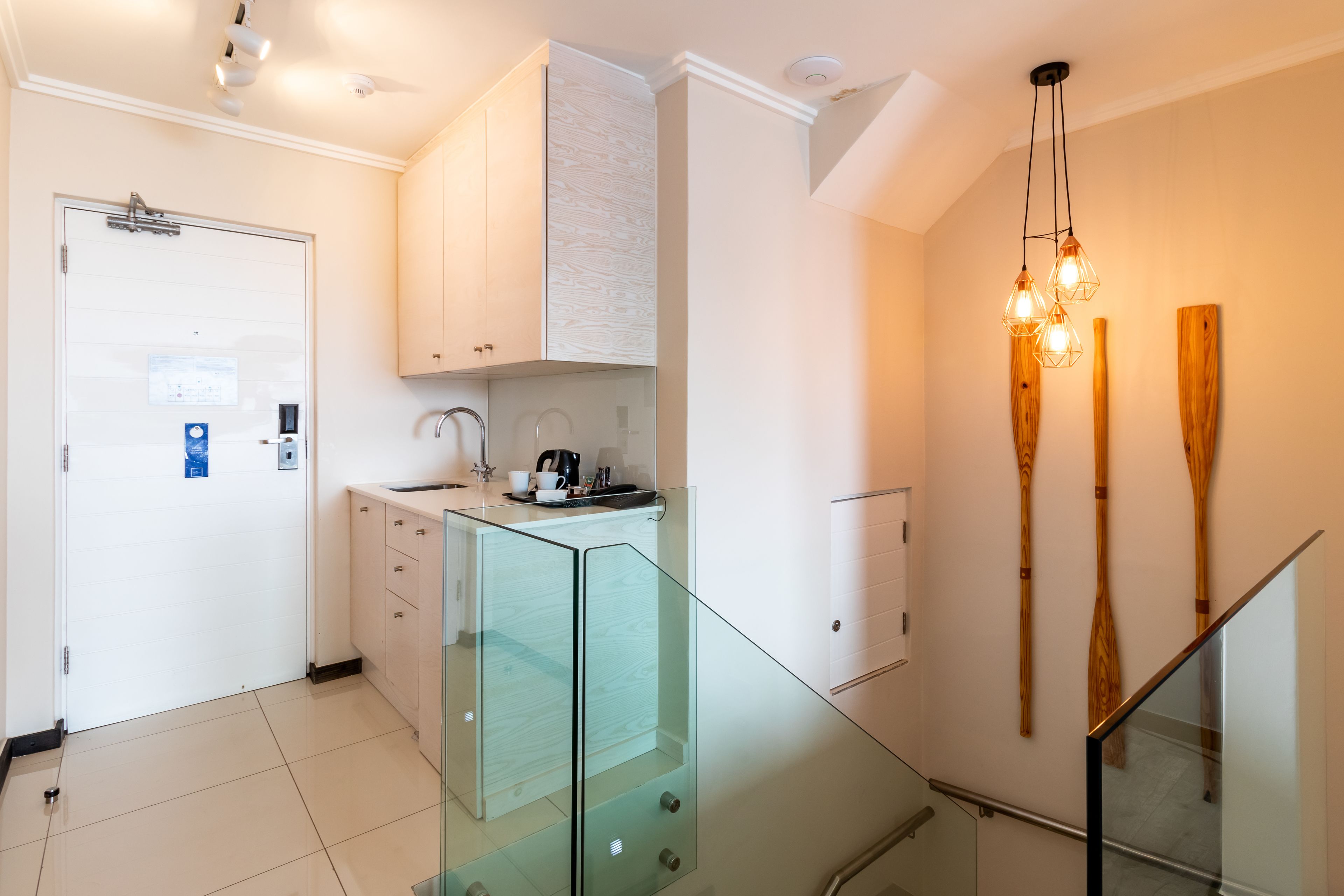 Een moderne keuken met een glazen wand, witte kasten en een houten plafondlamp.