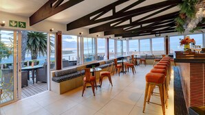 A modern restaurant with a terrace, seating area, and large windows offering ocean views. - Protea Hotel by Marriott Mossel Bay (Mossel Bay)