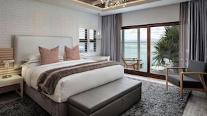 A modern bedroom with a large bed, a nightstand, a chair, and a view of the sea. - Protea Hotel by Marriott Mossel Bay (Mossel Bay)