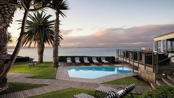 A pool area with lounge chairs and a view of the sea.