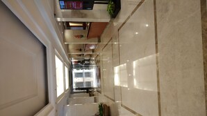 Un pasillo de hotel amplio y bien iluminado, con suelo de mármol, plantas en macetas y una zona de recepción con pantalla digital.